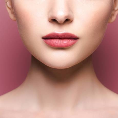 cropped view of young woman with lipstick on lips on pink